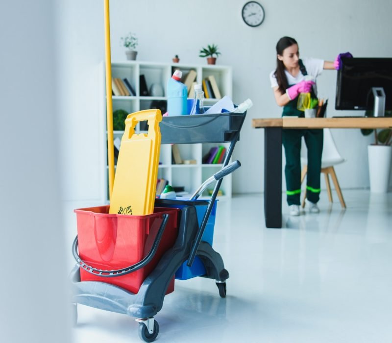 young-female-janitor-cleaning-office-with-various-cleaning-equipment.jpg